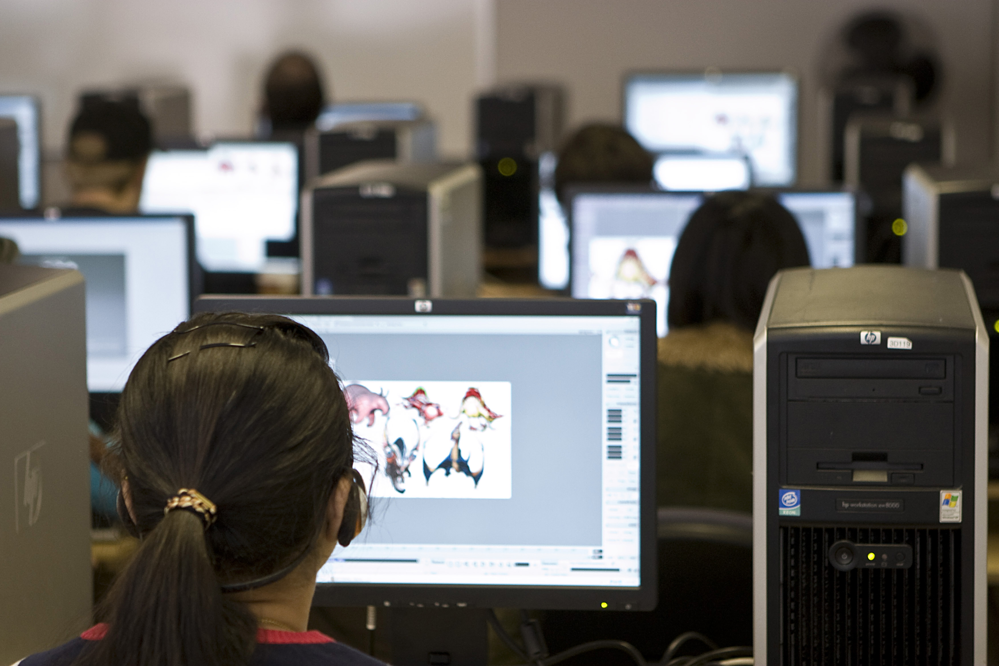 Several students sit behind computers in a computer lab operating a digital art program