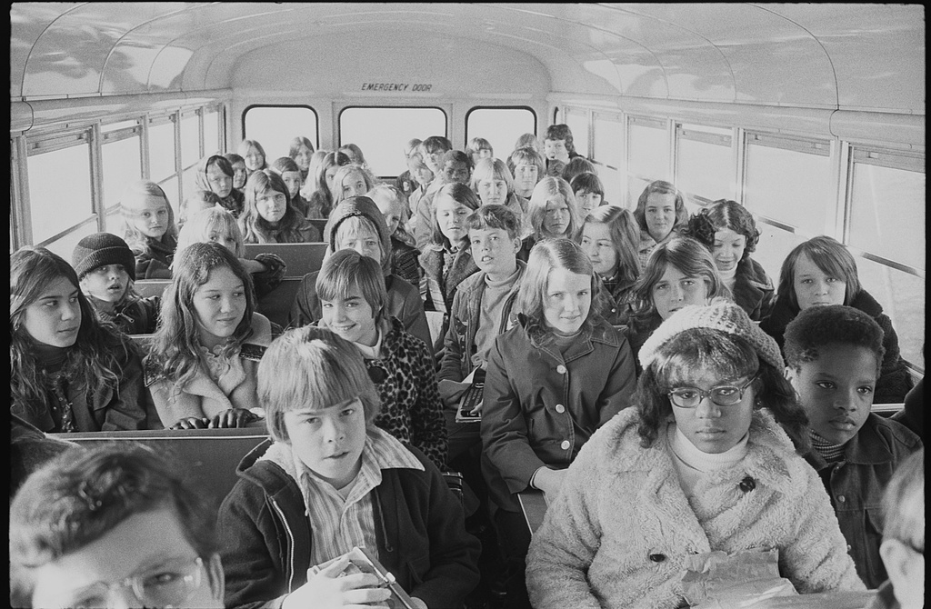 This image is of school age femme-presenting individuals crammed into a bus all wearing coats.