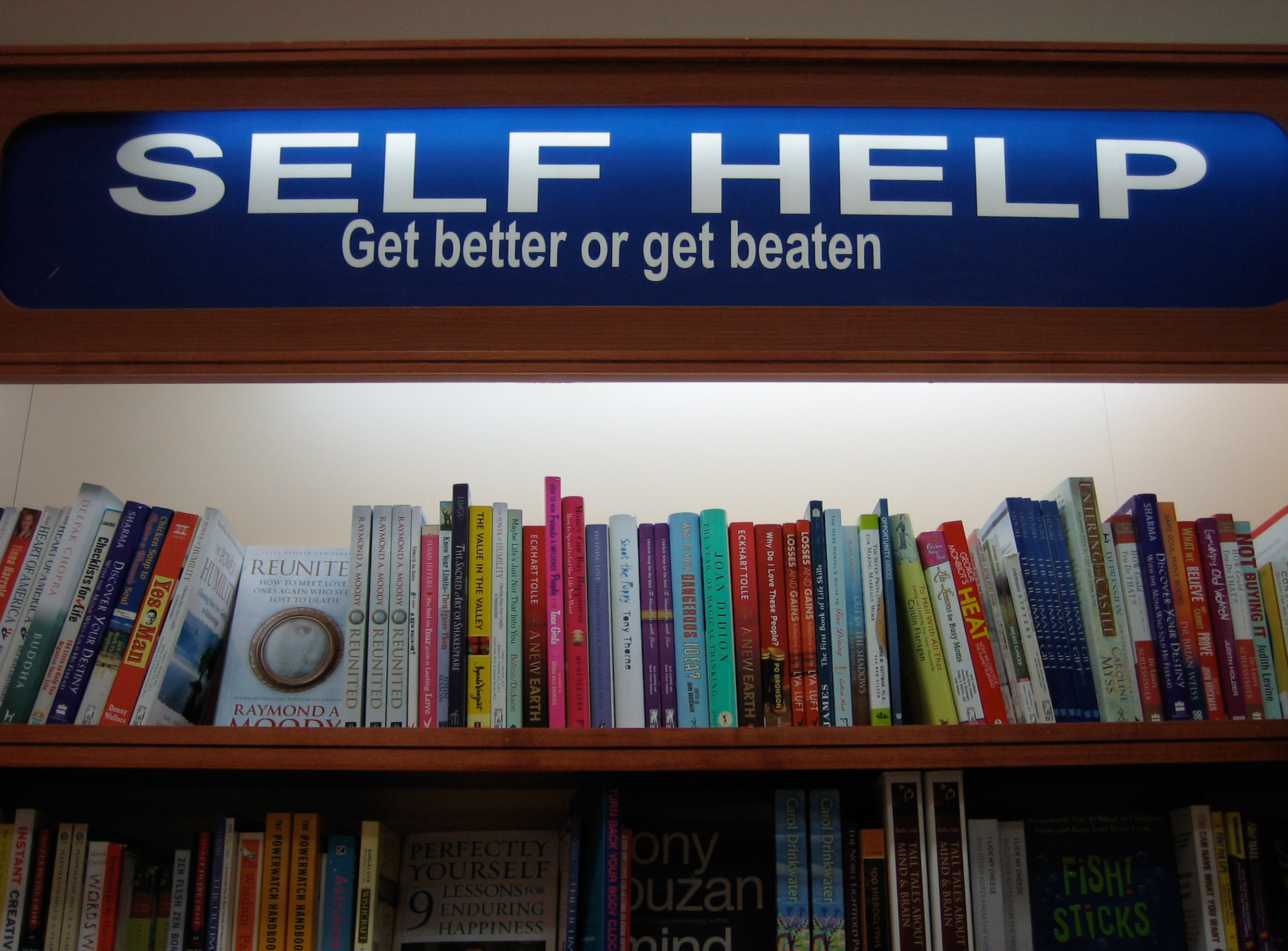 This is an image of the 'self help' section of a library with a sign that says 'Get better or get beaten'