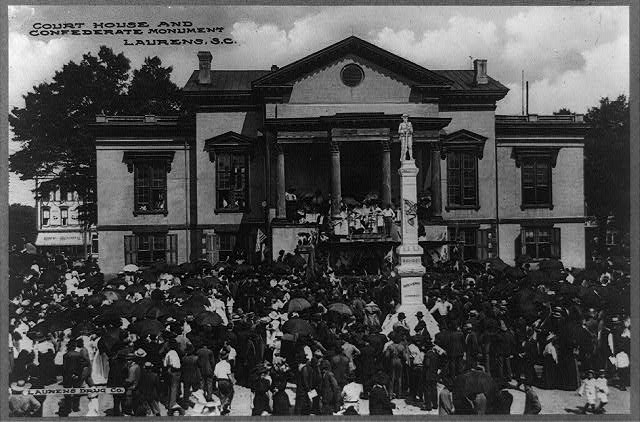 A large crowd gathers with umbrellas in the rain outside of a courthouse in this black and white photo