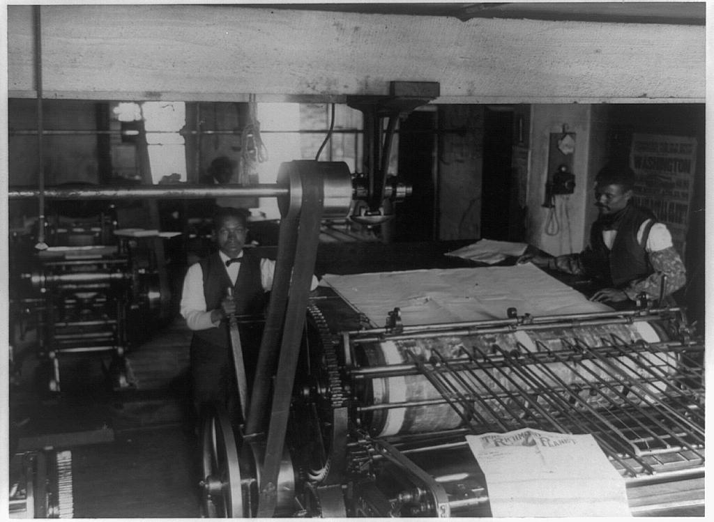 two black men work a printing press in this black and white photograph