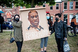 Image of 3 individuals, wearing masks, holding a poster of George Floyd's face and name.