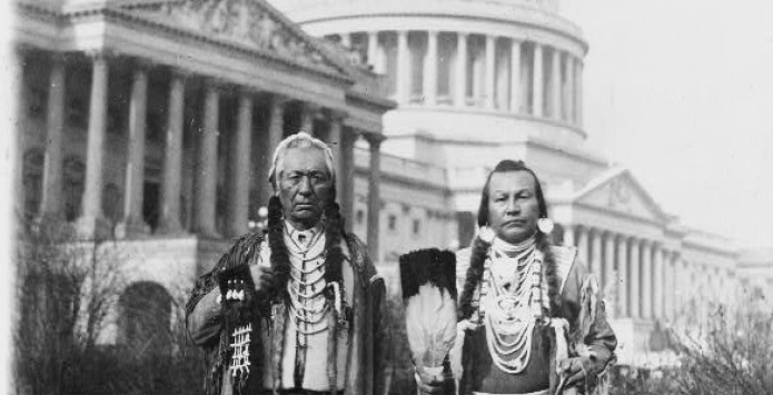 Two Native Americans in traditional Native American clothing standing in the front of the US Capitol Building