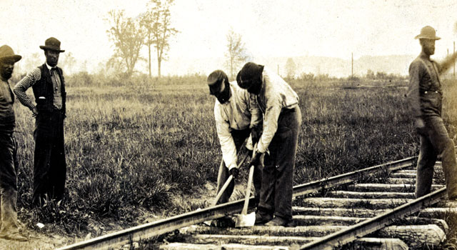 Two men working on a railroad while three other men look on