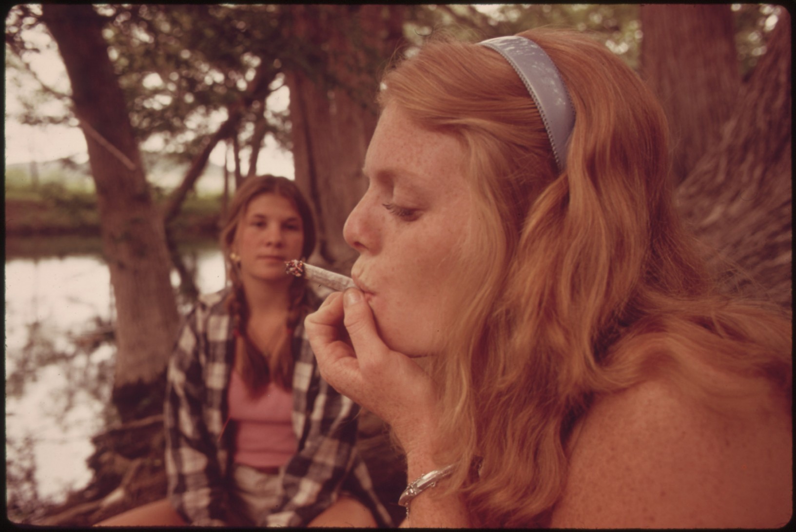 two teenagers smoke a marijuana cigarette in a park